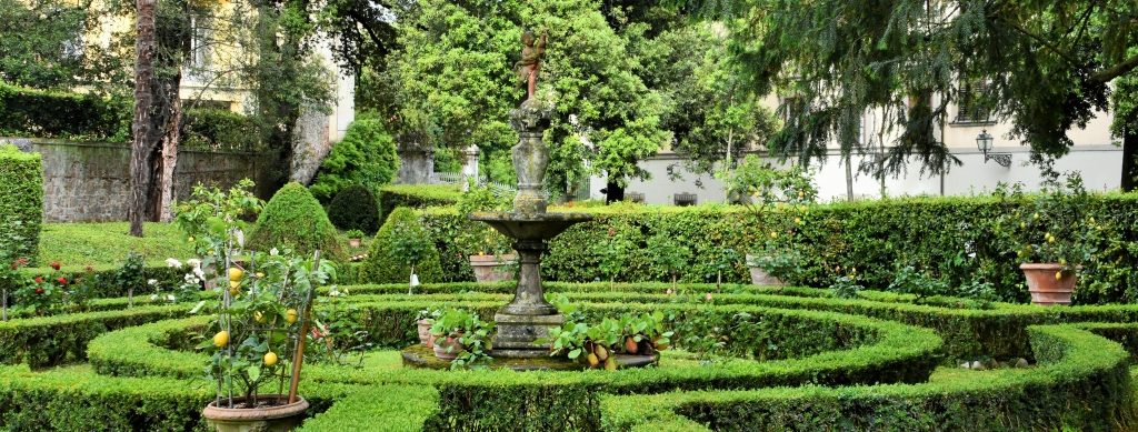Giardino con siepe tagliata in modo geometrico, statua al cento e vasi con limoni.