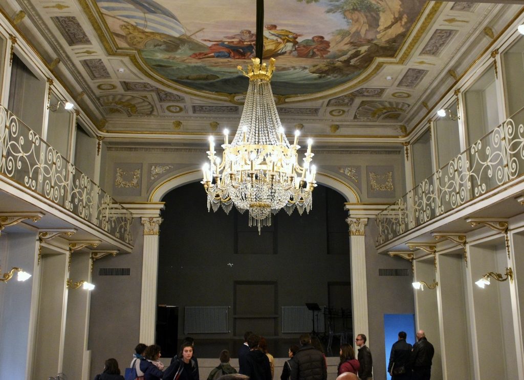 Teatro di colore bianco con soffio affrescato e lampadario al centro.