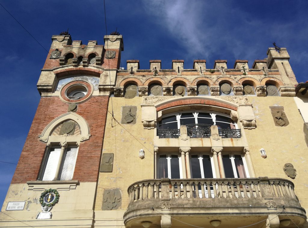 Edificio con merli, una terrazza con balaustra in pietra, due serie di grandi bifore, intonaco giallo con stemmi. Attaccata una torretta con una bifora e sopra una finestra tonda, intonaco rosso scuro.