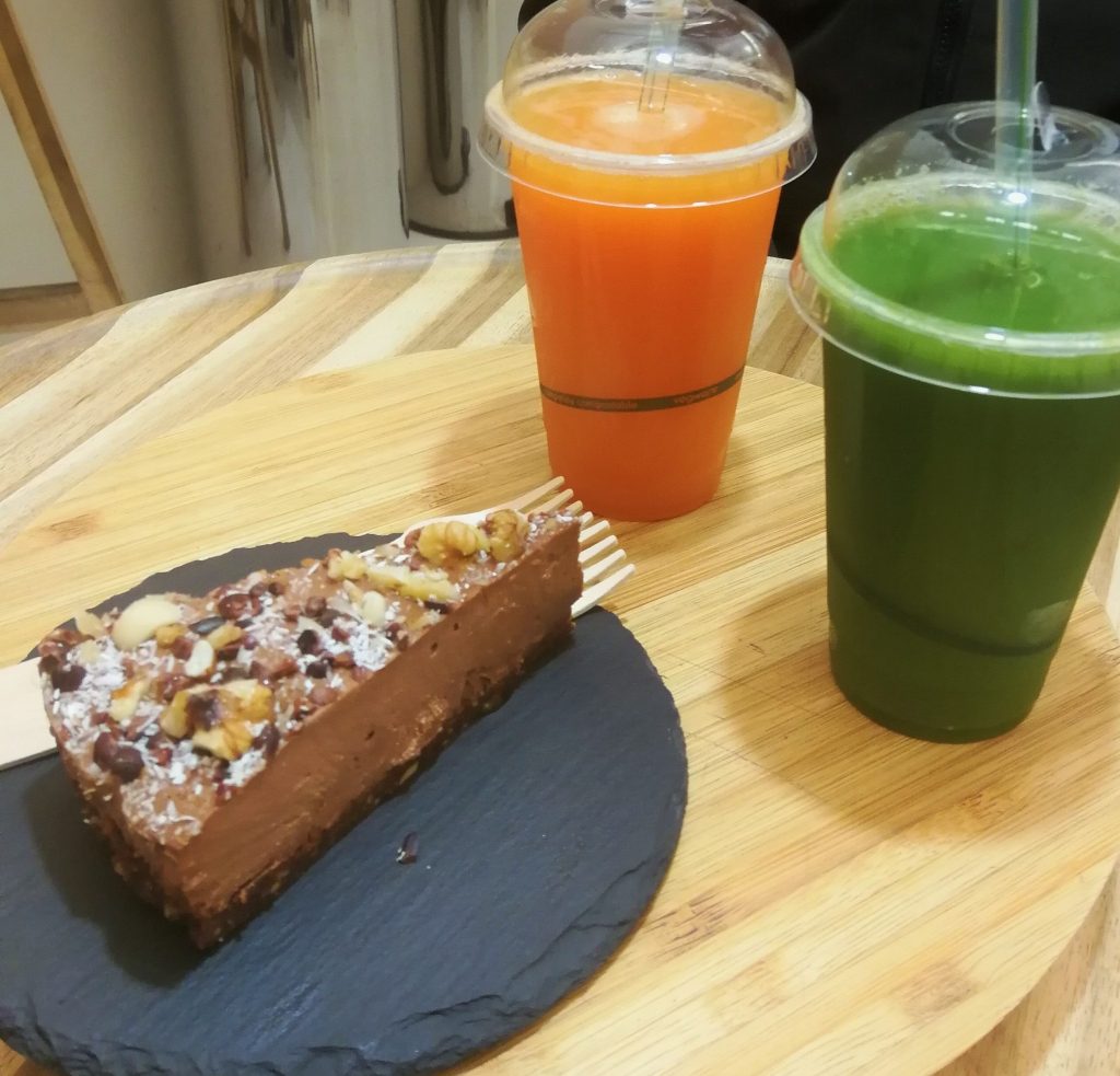 Torta su piatto nero con due centrifughe, una arancione e l'altra verde. Tavolo di legno chiaro.