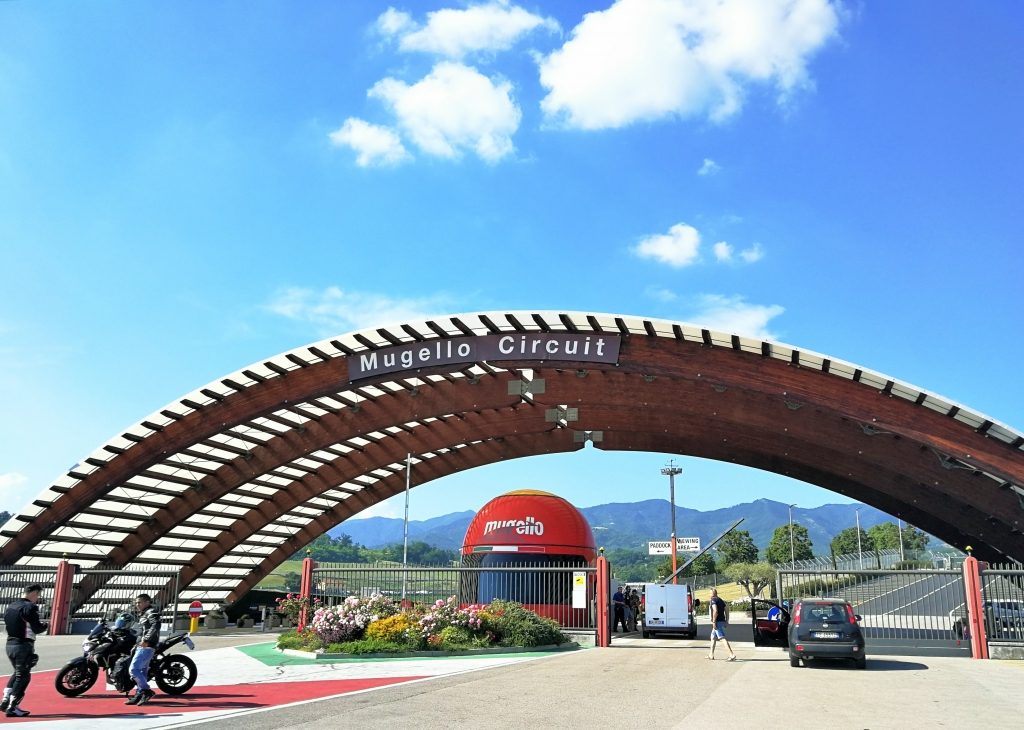 Ingresso del Mugello CIrcuit: strada con auto, grande struttura a volta che disegna un portale e sotto la postazione della polizia a forma di casco integrale rosso. 