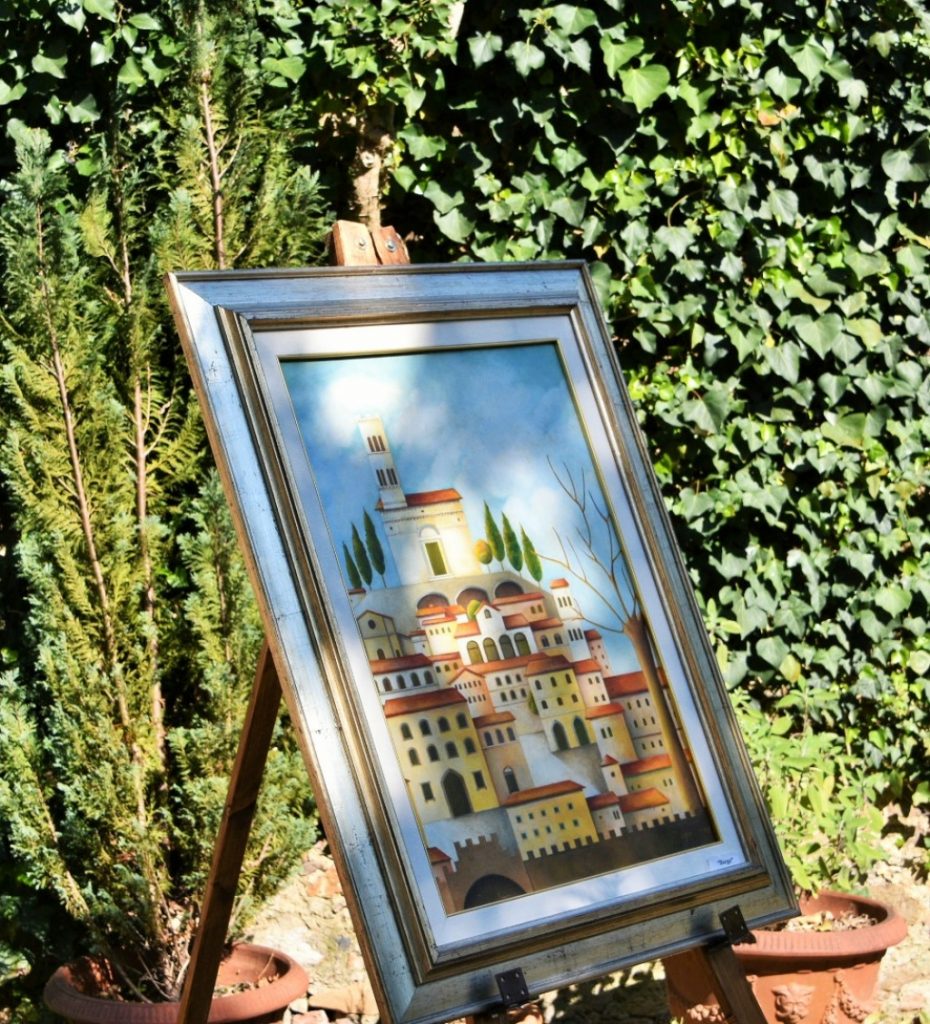 Quadro su cavalletto con rappresentati dei palazzi, sfondo una siepe e due vasi.
