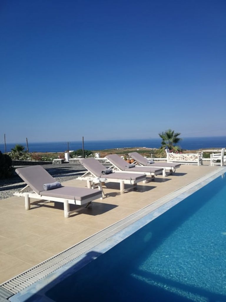 Piscina con lettini, sullo sfondo alcuni alberi e il mare.