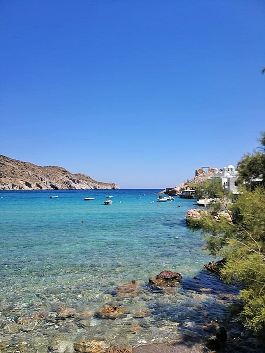Acqua cristallina con vegetazione a sinistra e case di pescatori; alcune barche.