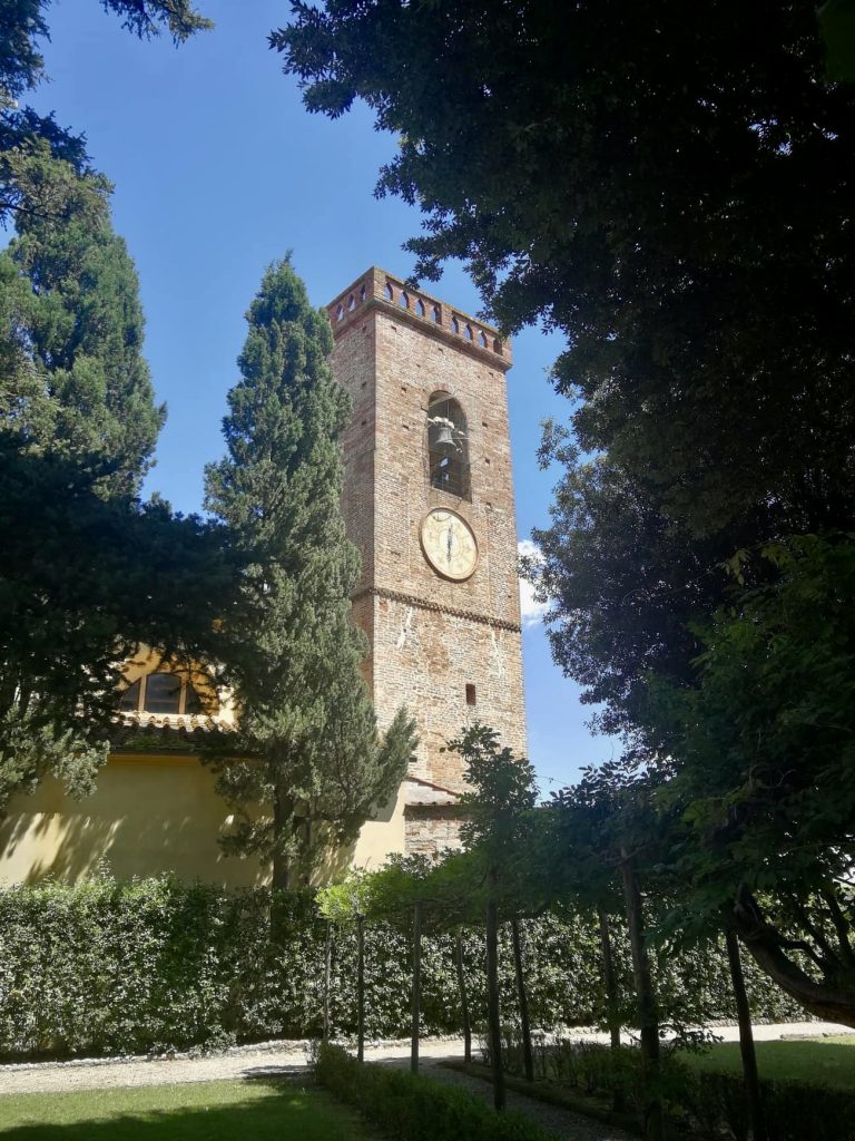 Campanile in mattoni, orologio e piante, alberi.