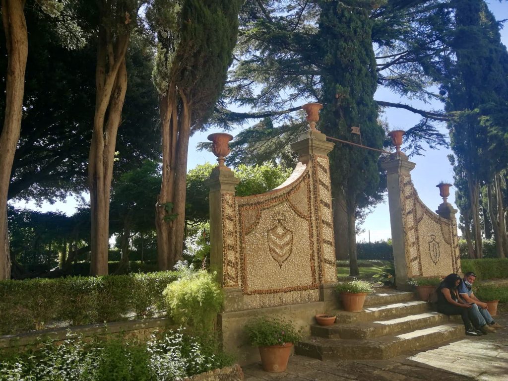 Giardino con alberi e ingresso con porte a mosaico e vasi in terracotta.