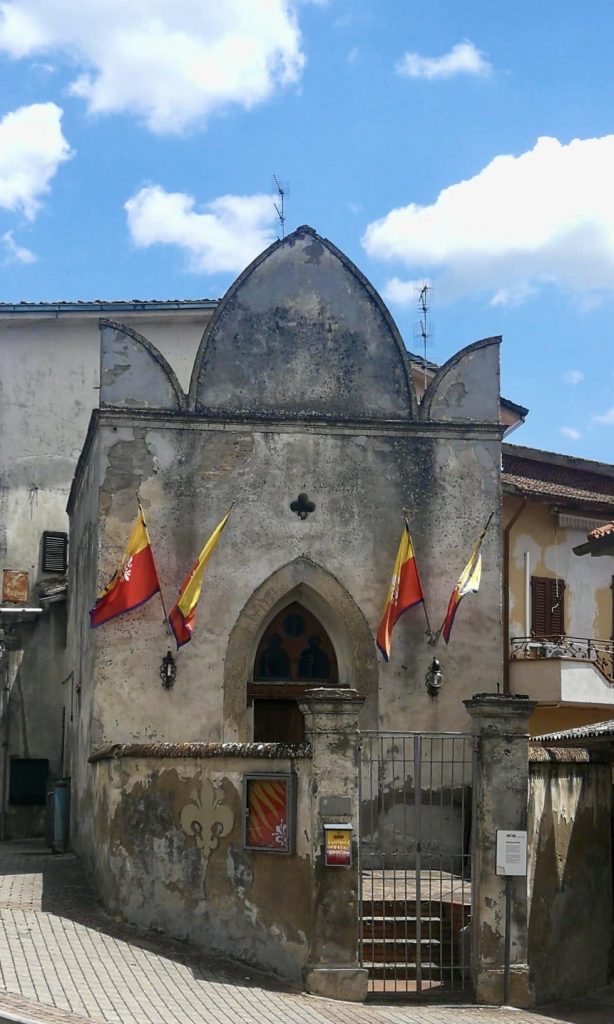 Piccola chiesa ad angolo, grigia e con bandiere rosse e gialle.