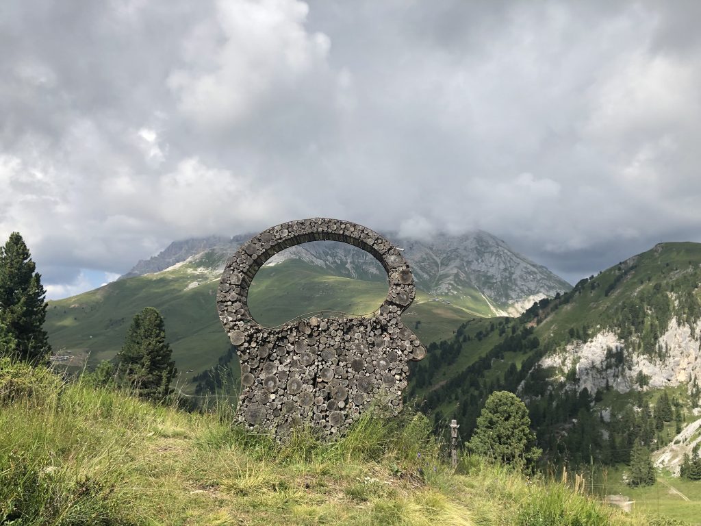 Panorama sulle dolomiti con montagne, boschi e prati verdeggianti; al centro un'opera d'arte, Mind's Eye.