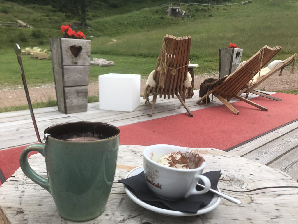 Particolare di due cioccolate calde nella parte esterna di uno chalet, fiori e sedie di legno.