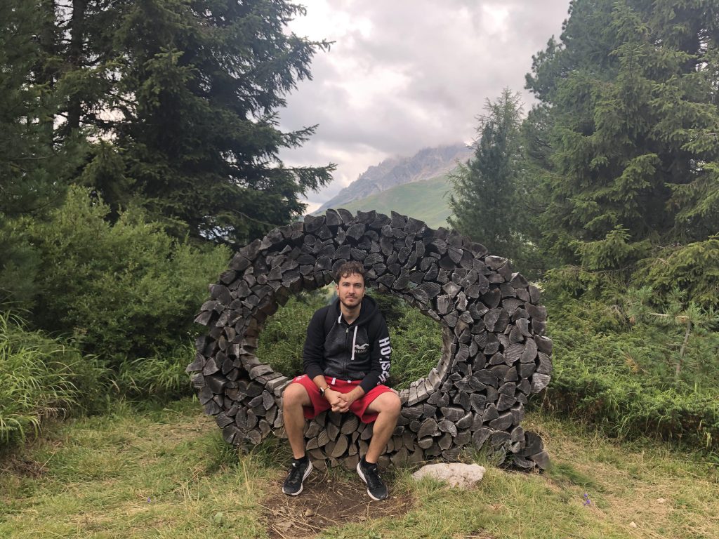 Lorenzo seduto sull'opera Messa a fuoco sul Latemar, con boschi e montagne sullo sfondo.