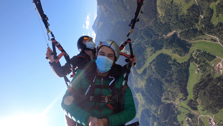 Acrobazia durante il volo in parapendio: Lorenzo al centro e il ragazzo pilota dietro, fili del parapendio, cielo e valle.
