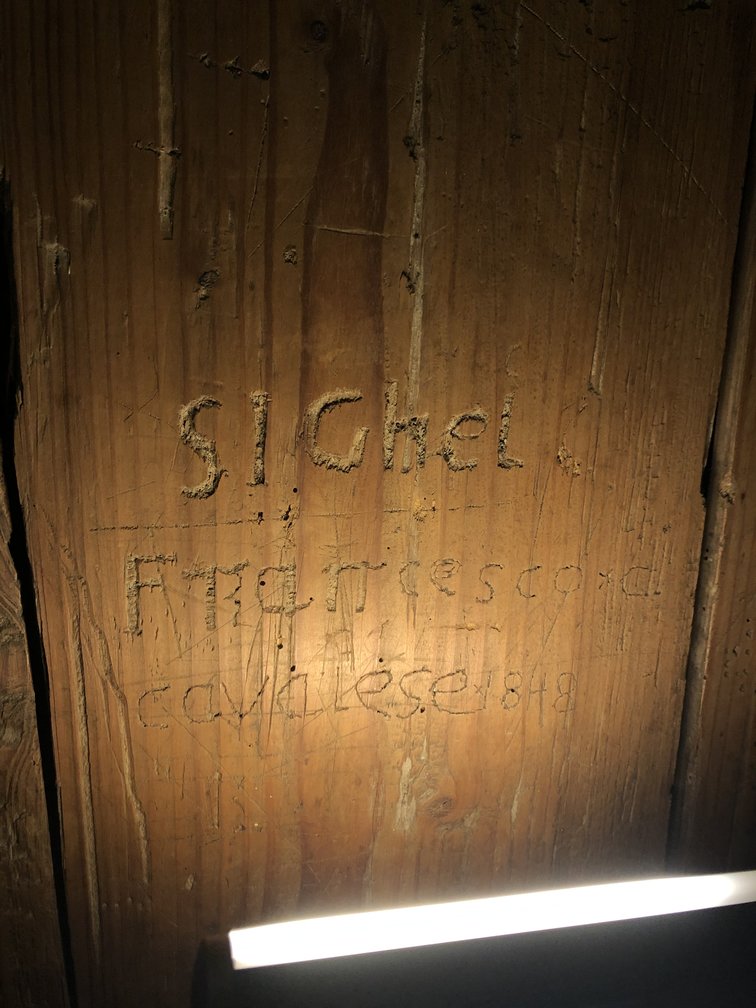 Scritta incisa nel legno, illuminata da una torcia.