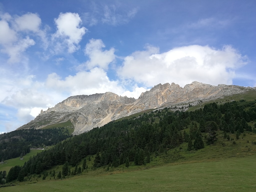 Latemar: catena montuosa, rocce chiare con cielo nuvoloso. Vista dal basso con boschi e prati.
