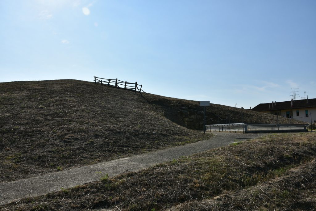 Collinetta di terra, cielo sereno, una strada che porta all'entrata della tomba.