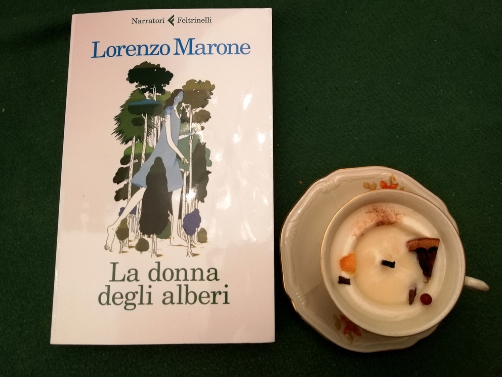 Copertina del libro La donna degli alberi con accanto una candela un po' consumata ricavata in una tazza da caffè con piattino.