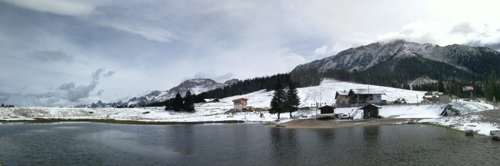 Paesaggio innevato: lago con case e montagne sullo sfondo.