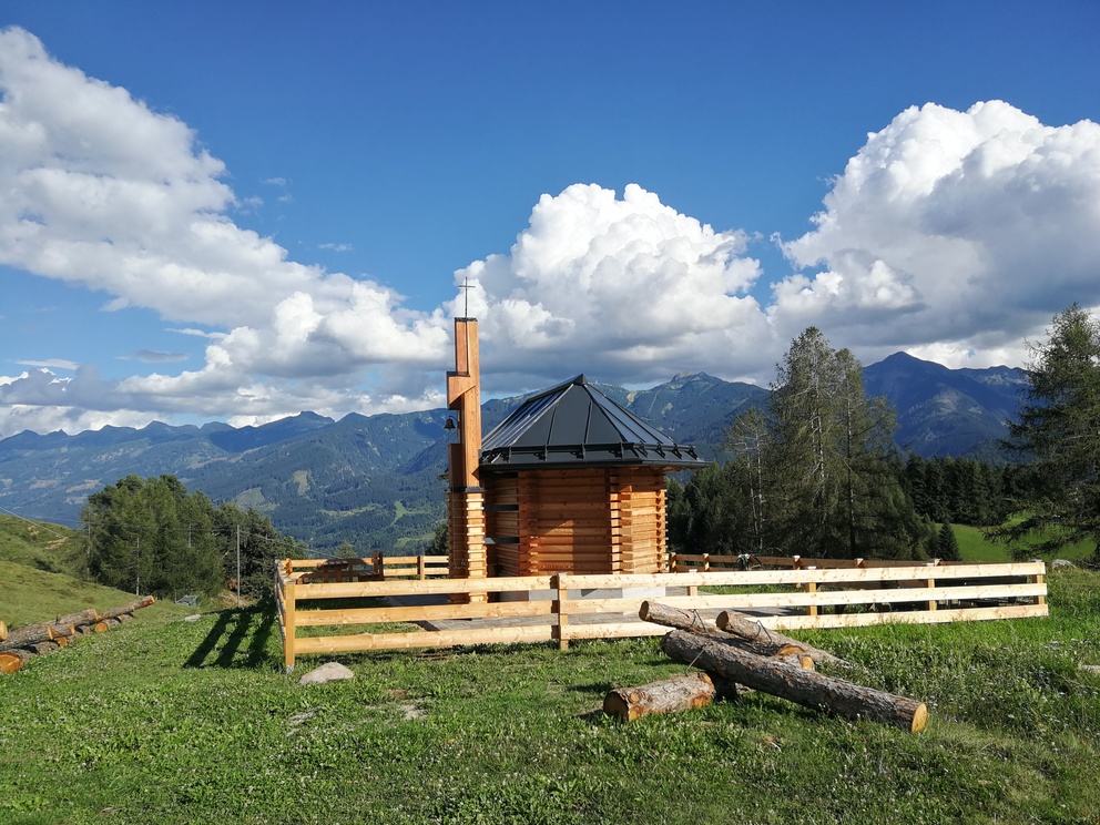 Chiesetta degli Alpini - staccionata, bandiere dell'Italia al vento, prati e panorama di montagne con alberi.