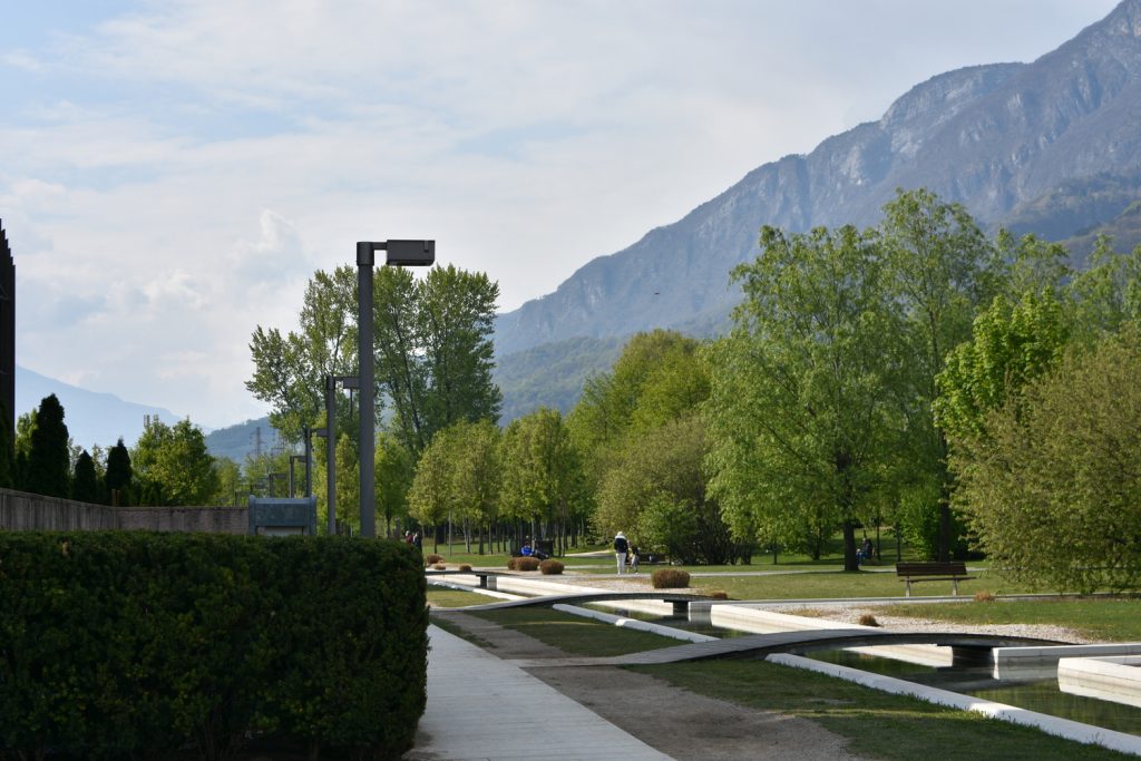 Giardini con specchio d'acqua, piccoli ponticelli, lampioni e montagne sullo sfondo.