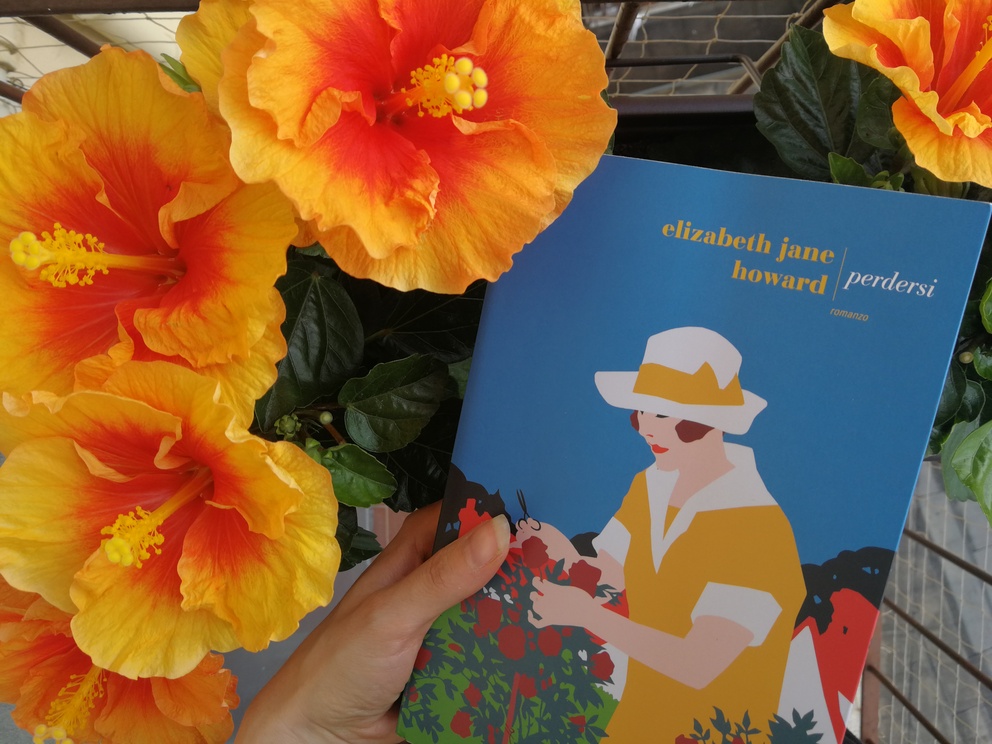 Copertina del libro Perdersi in un vaso di fiori arancioni con grandi pistilli gialli; si intravede una ringhiera marrone e una mano che tiene il libro.