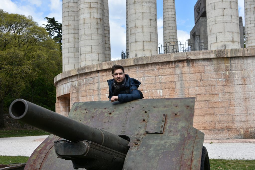 Lorenzo appoggiato su un cannone di fronte alle colonne del mausoleo a cesare battisti.