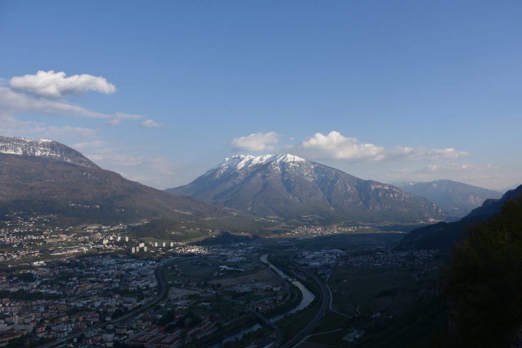 Panorama sulla città di Trento al tramonto, dall'alto, con montagne e fiume.