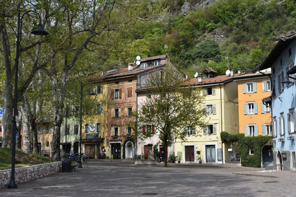 Piedicastello: piazza con case di diversi colori e alberi.
