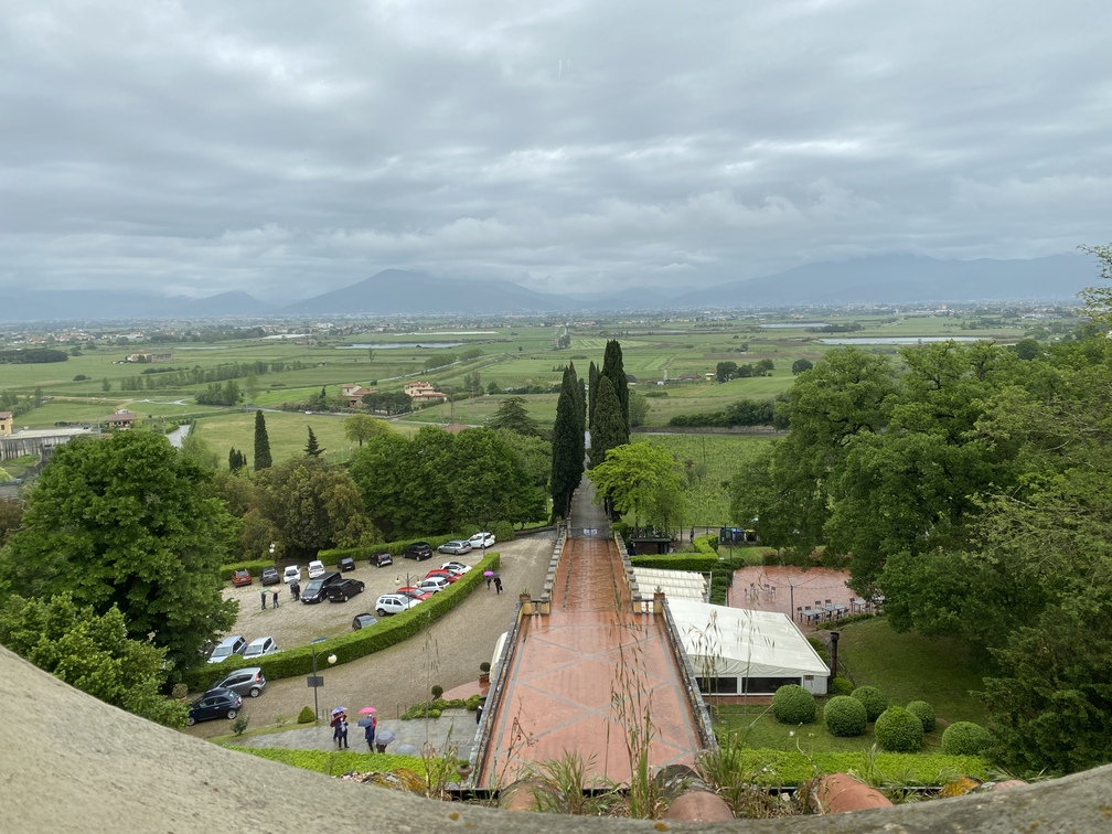 Villa Castelletti - panorama con vista su strada in salita, cipressi, parcheggio e prati e vegetazione, montagna in lontananza.