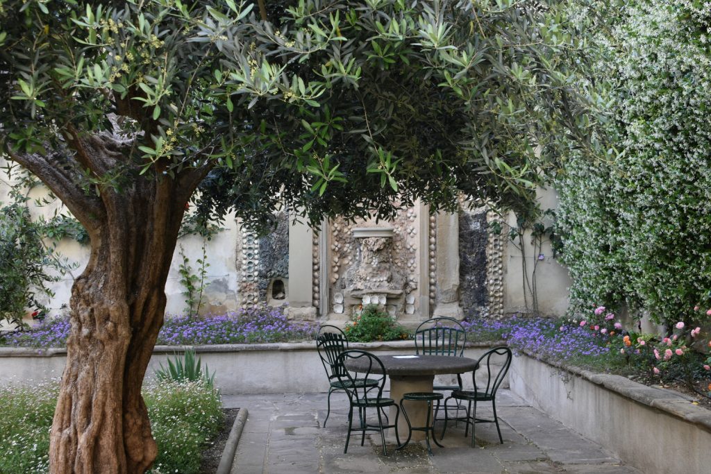 Palazzo Antellesi - cortile interno con tavolo e albero in primo piano, dietro fontana e fiori.