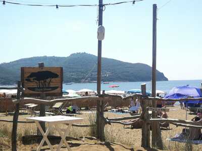 Bagno Baratti - insegna sul mare con ombrelloni, spiaggia, mare e promontorio sullo sfondo.