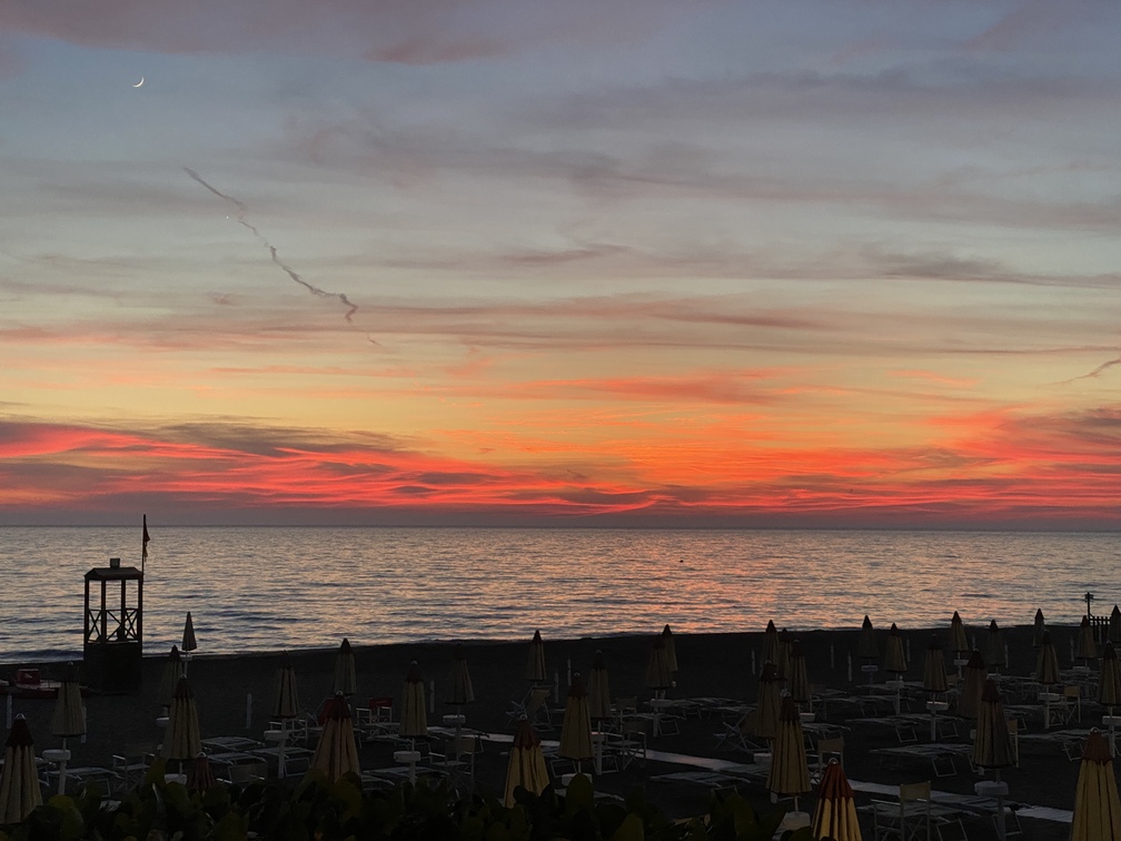 Tramonto a Castagneto Carducci con sole ormai scomparso nel mare, striature rossastre, mare, spiaggia con ombrelloni chiusi.