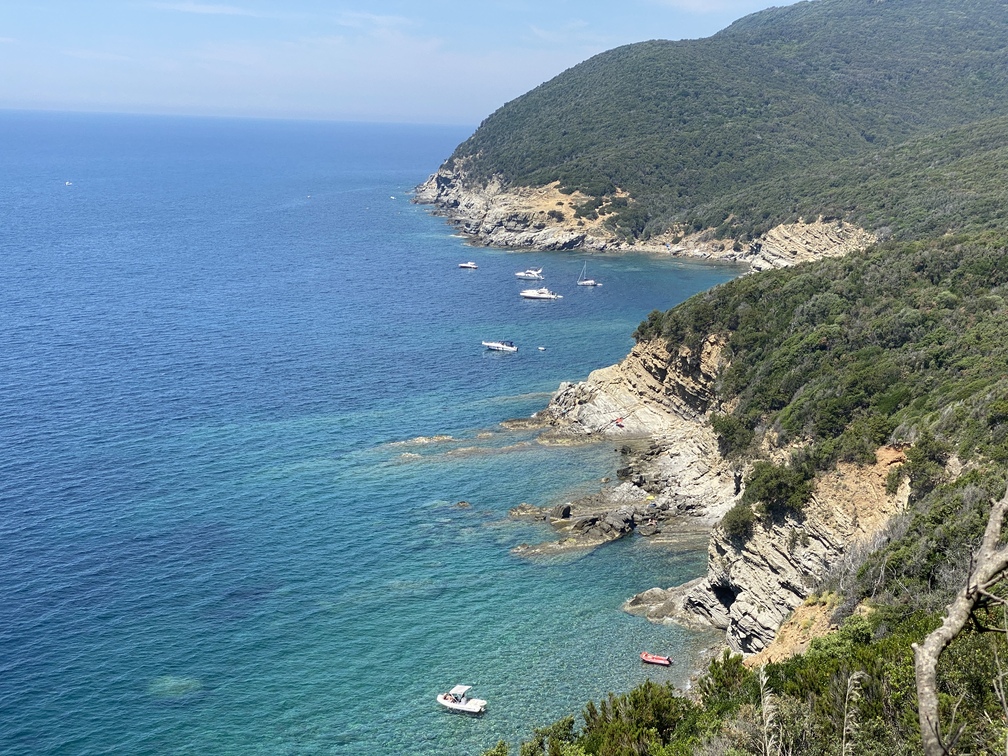 Panorama sulla costa di Populonia con mare azzurro, rocce, barche e bosco.