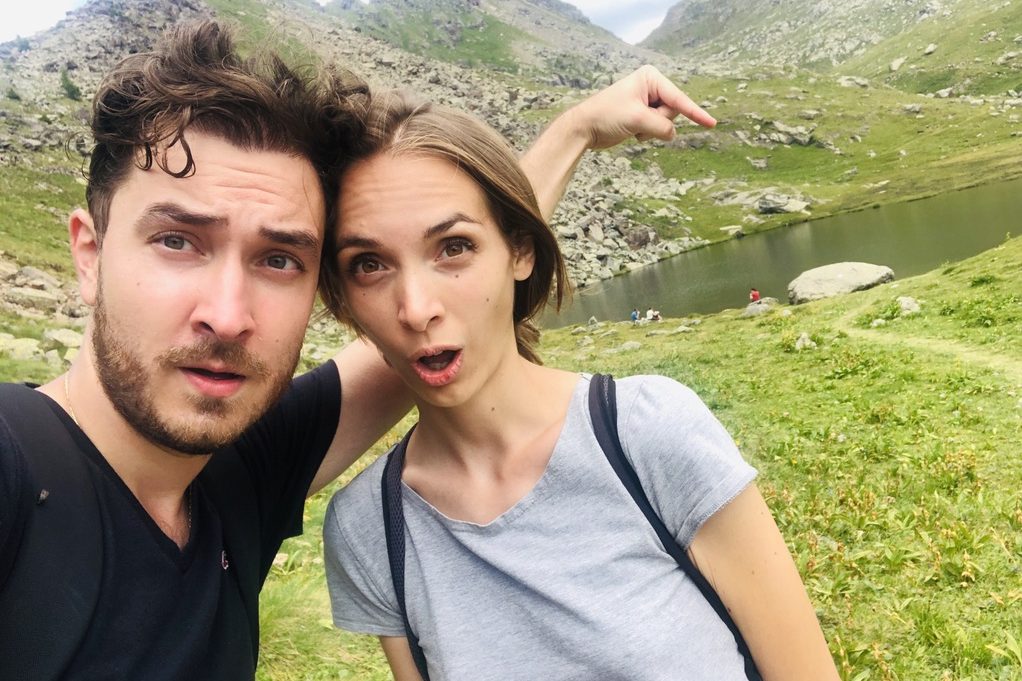 Lorenzo e Federica con facce sorprese, indiano un lago di montagna, rocce e prati verdi.
