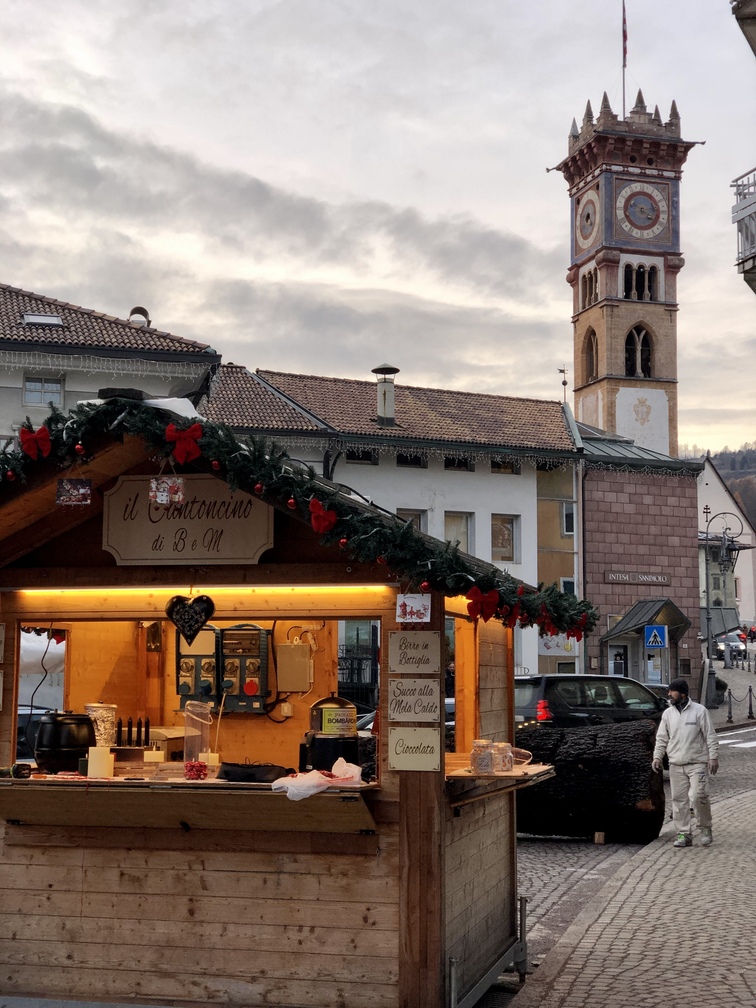 Mercatino di Natale 2025 di Cavalese - casina con lo stand del Canton e campanile di San Sebastiano.