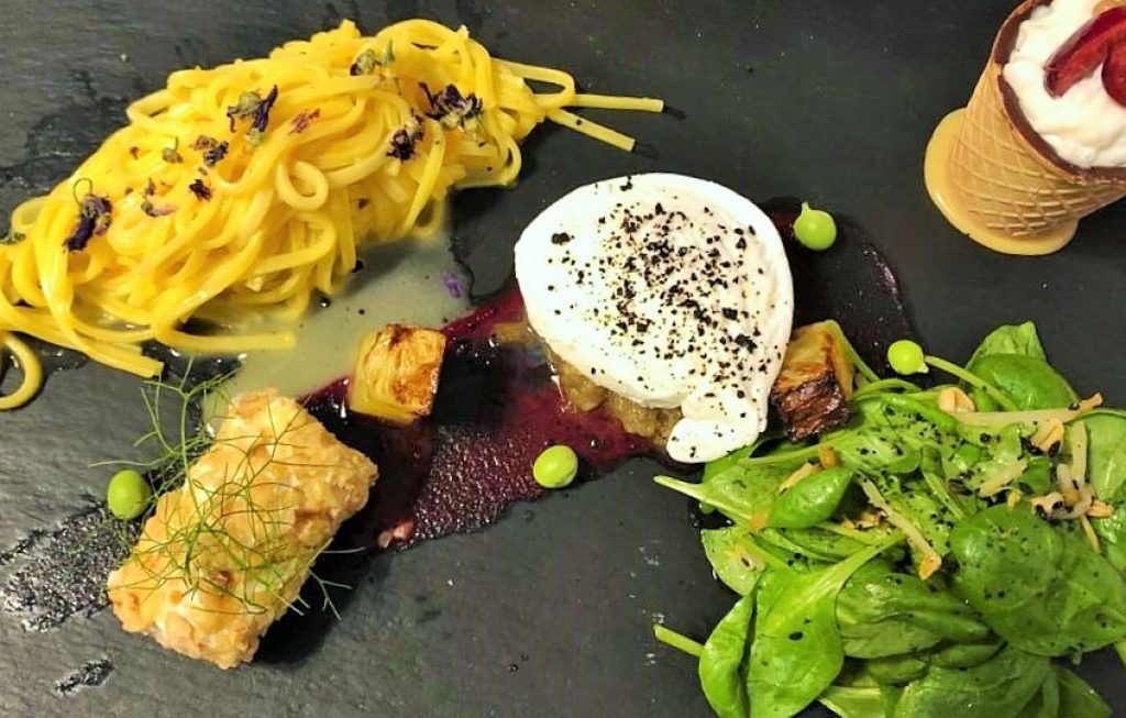 Piatto nero con spaghetti, al centro uovo e barbabietola rossa , a destra insalata di spinaci e germogli di soia e in alto un dolce con fragole.