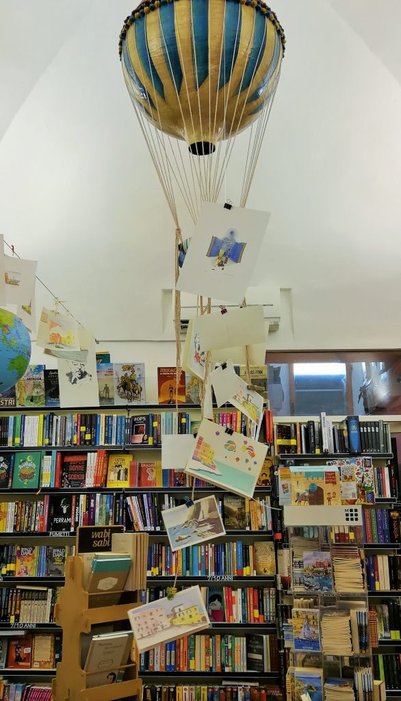 Libreria con una mongolfiera con appese delle cartoline con disegni colorati.