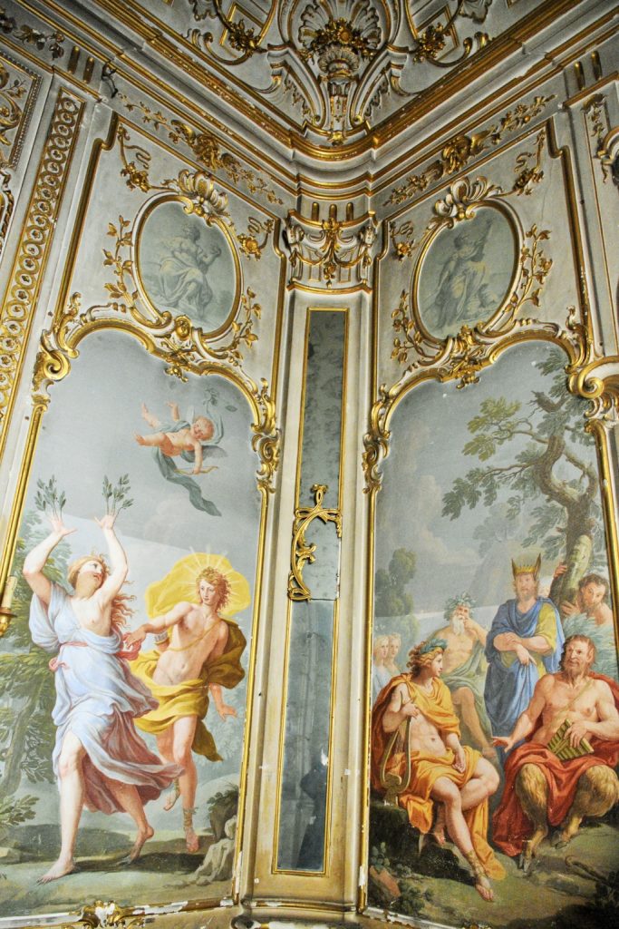 Affreschi raffiguranti Apollo e Dafne e Apollo e Marzia con re Mida, stucchi dorati e specchio nell'angolo.