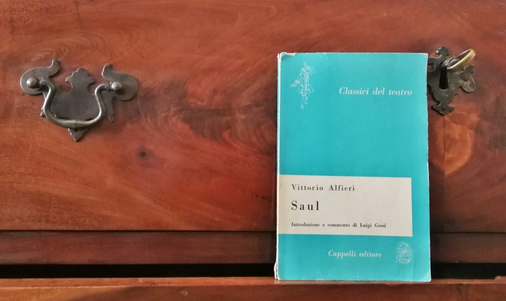 Il libro di colore azzurro e bianco sopra un legno scuro ma caldo con venature, una chiave e una manopola di un cassetto.