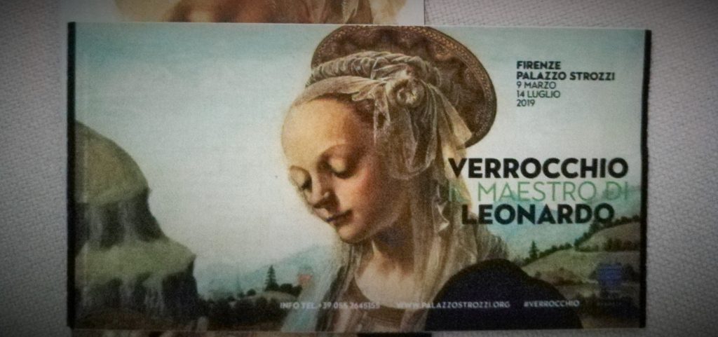 Biglietto della mostra con in primo piano un dettaglio di un dipinto di Andrea Verrocchio, il viso della Madonna.