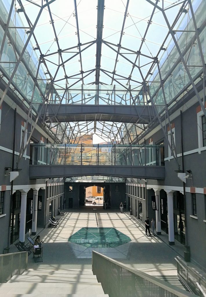 Ingresso del museo con una grande struttura in vetro trasparente che fa da tetto a due edifici collegati da una ponte sospeso al primo piano.