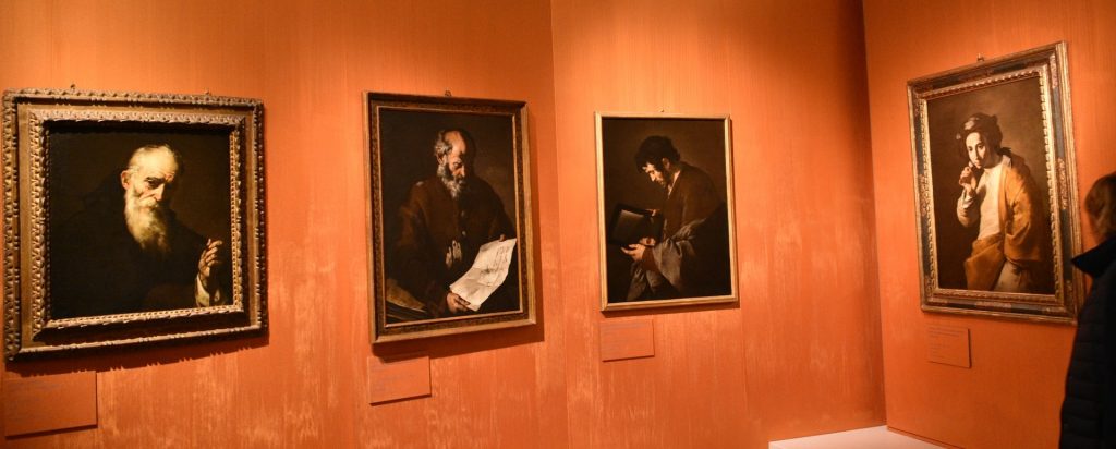 Quattro dipinti della mostra, raffiguranti saggi e allegorie dei sensi; i dipinti sono appesi a pareti di colore arancione.