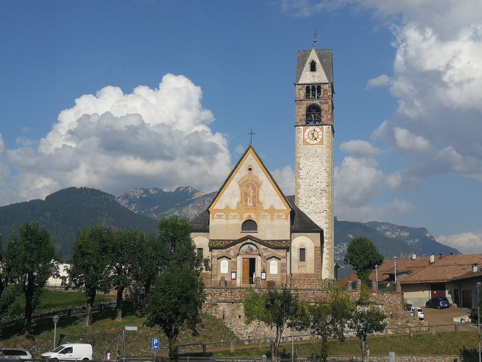 Chiesa di Carano, con montagne, alberi e nuvole.