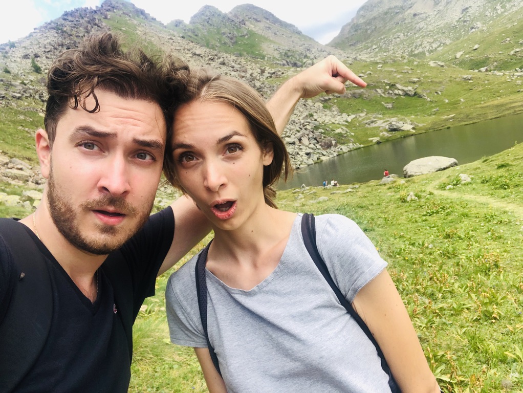 Lorenzo e Federica con facce sorprese, indiano un lago di montagna, rocce e prati verdi.