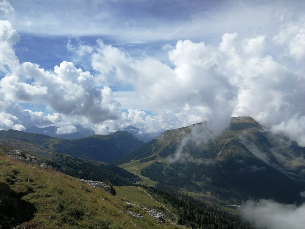 Panorama dal Latemar: montagne verde con prati e boschi. Molte nuvole.