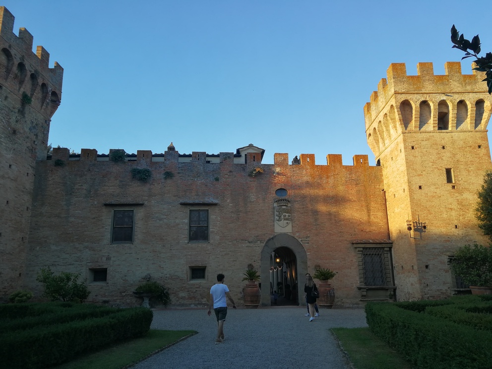 Castello di Oliveto - vista dal cortile interno con due torri merlate e palazzo, luce del tramonto, siepi.