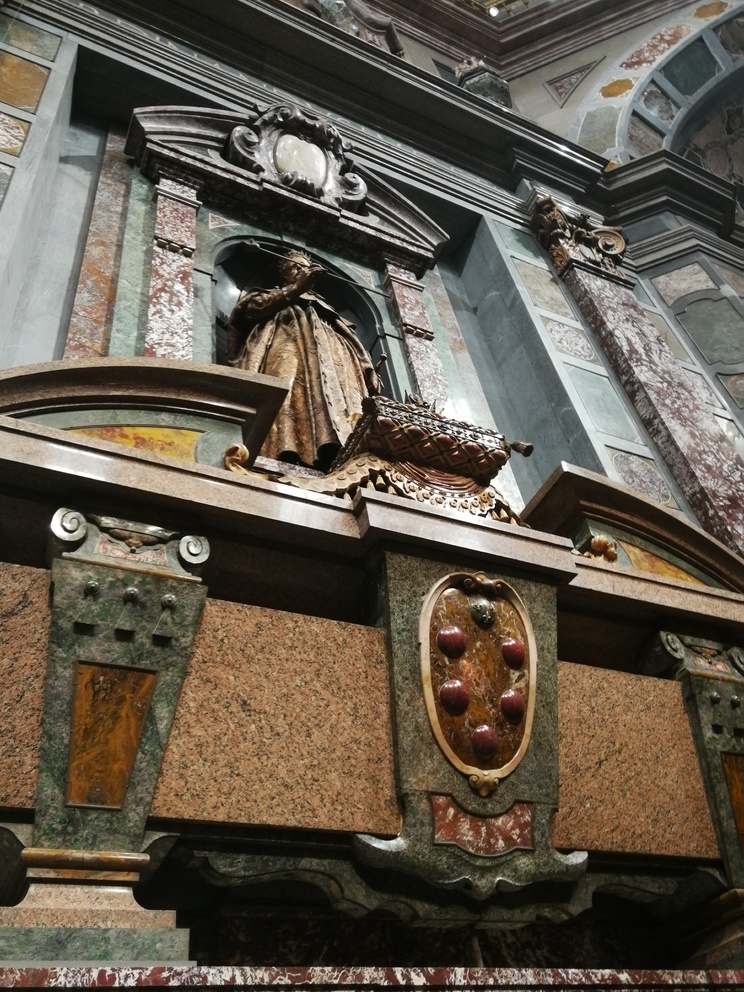 Cappelle Medicee: Cappella dei Principi; primo piano di un sarcofago con stemma mediceo e sopra statua.
