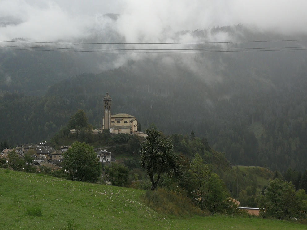 Castello di Fiemme- vista dalla valle, con nuvole basse, chiesetta e campanile.