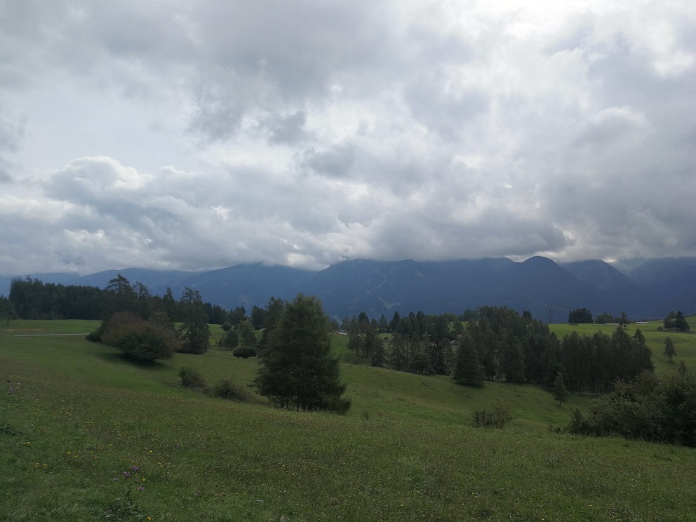 Giro del Solombo - prati con pochi alberi, montagne e cielo nuvoloso.