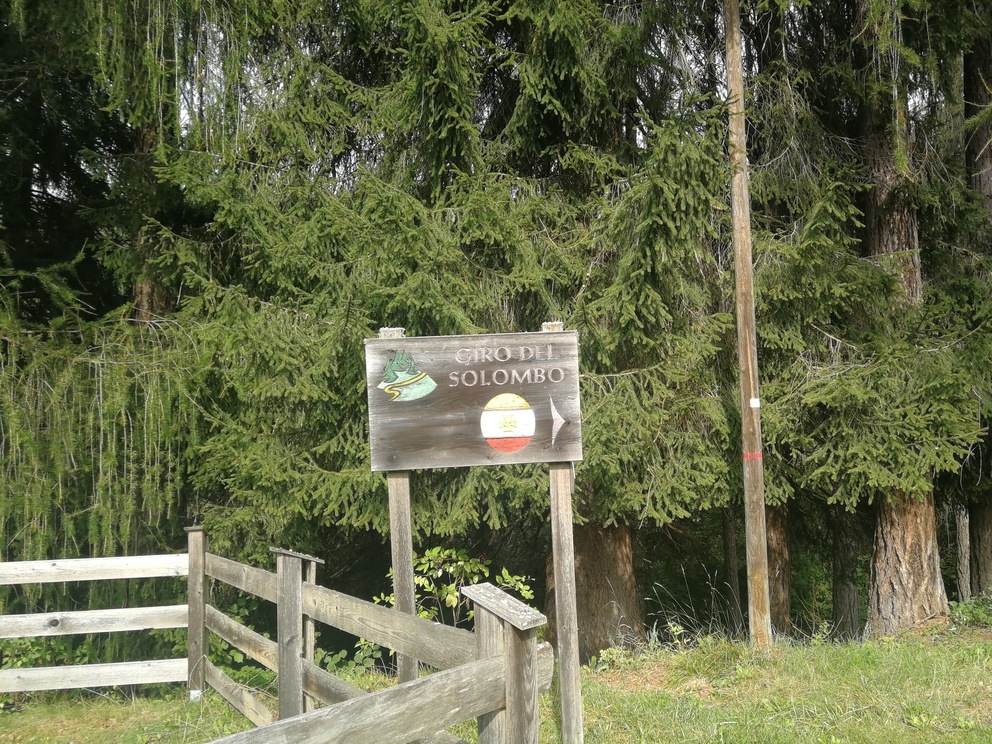 Giro del Solombo - cartello esplicativo con freccia, alberi e bosco.