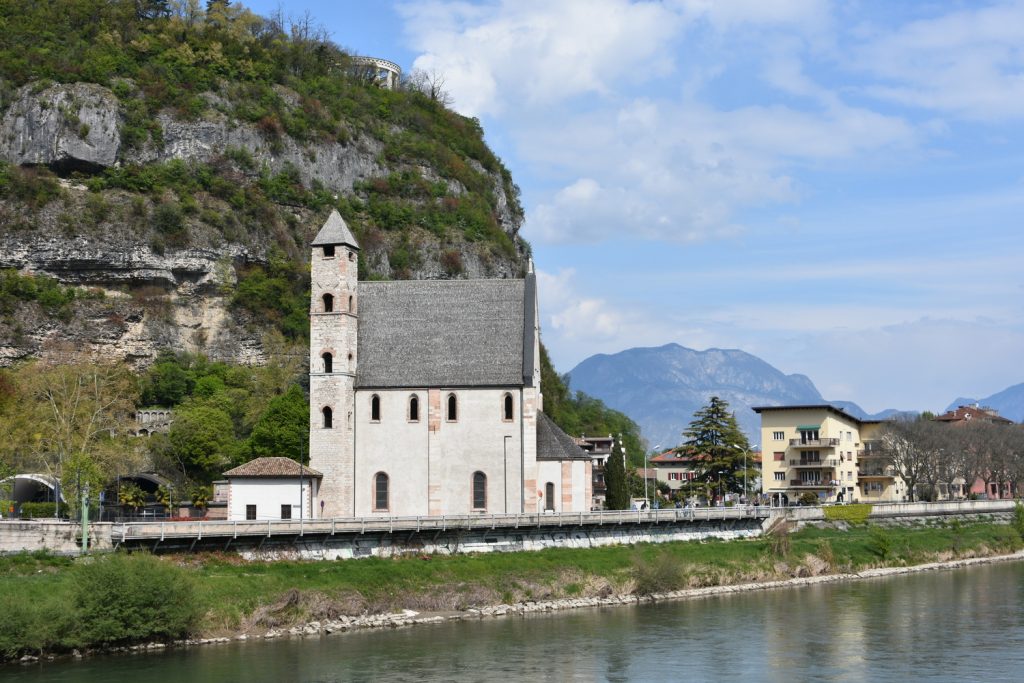 Chiesa Santa Apollinare di lato con campanile, fiume Adige e dietro collina.